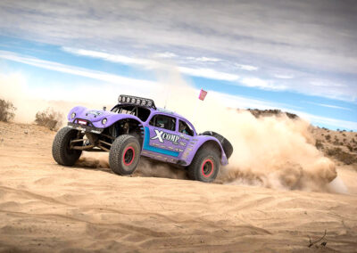 All-terrain vehicle racing off-road desert scene with dust cloud, featuring a purple custom off-road vehicle in action.
